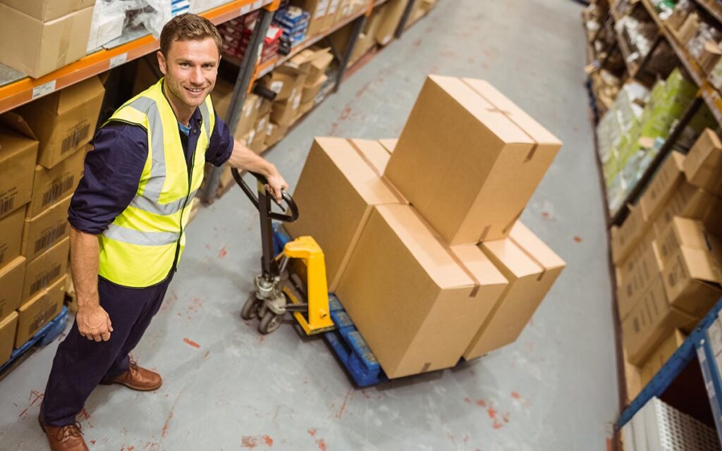 Worker,With,Trolley,Of,Boxes,Smiling,At,Camera,In,A